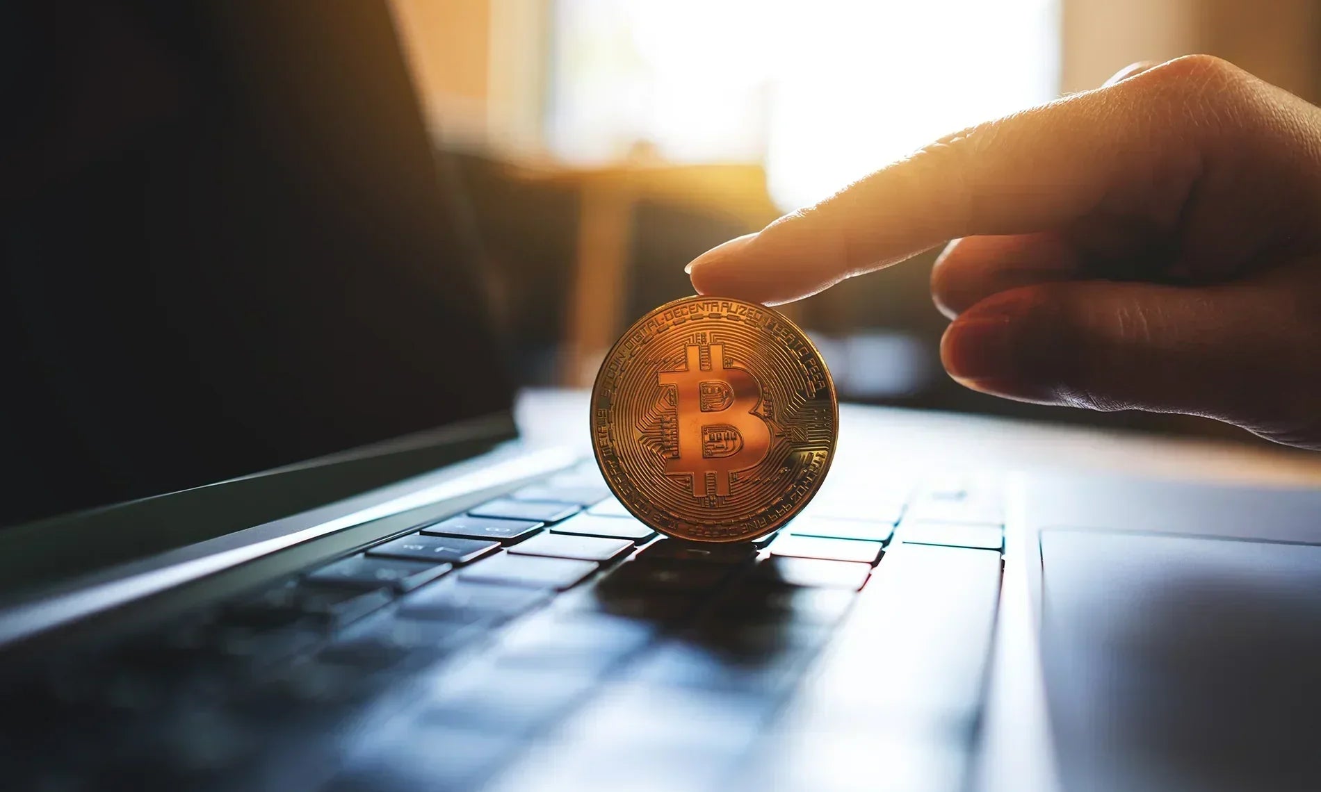 Bitcoin held by an hand atop a laptop keyboard.