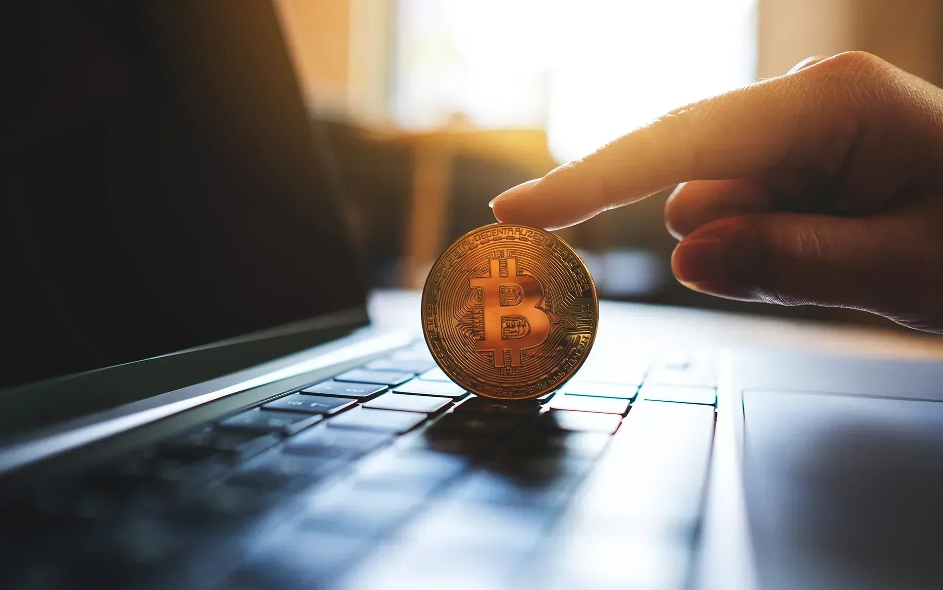 Bitcoin held by an hand atop a laptop keyboard.